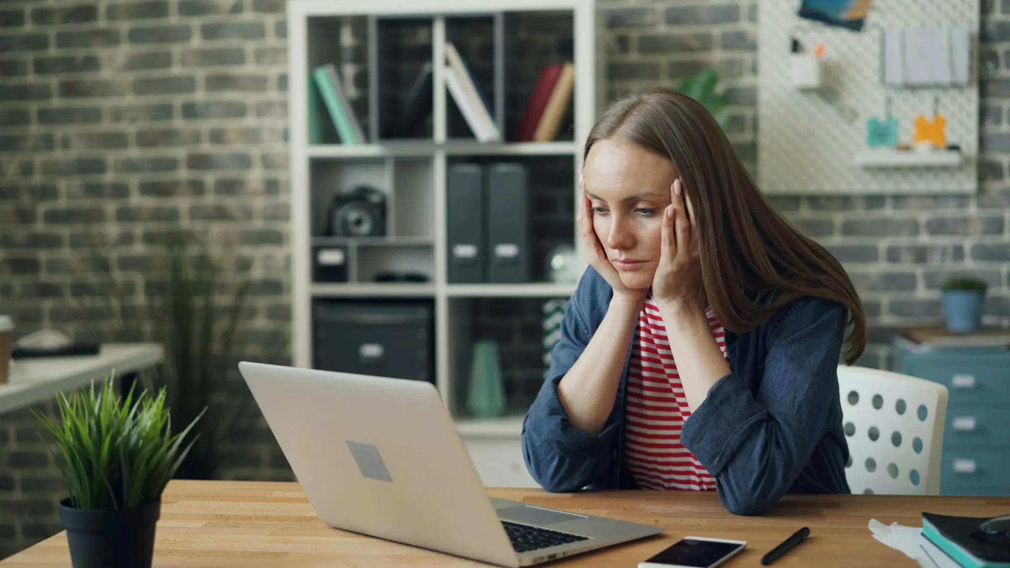 Small business owner at a desk in her studio office, chin in hands, weighing up a business loan offer on her laptop